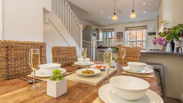 A dining area with a wooden table set for a meal, surrounded by wicker furniture and white plates. - Driftwood Cottage, Brancaster, Norfolk (King's Lynn)