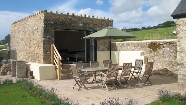 An outdoor patio with stone walls, a table, and chairs. - Cosy cottage with large garden in gorgeous rural setting. (Dalwood, Devon)