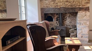 A cozy room with a stone fireplace, wooden furniture, and a bookshelf with board games. - Cosy cottage with large garden in gorgeous rural setting. (Dalwood, Devon)