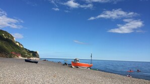 A pebble beach with boats, a clear sky, and a calm sea. - Cosy cottage with large garden in gorgeous rural setting. (Dalwood, Devon)