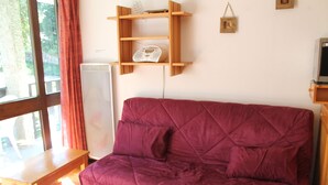Une pièce avec une table en bois, un canapé violet, un radiateur blanc et une étagère sur laquelle se trouve une radio.
