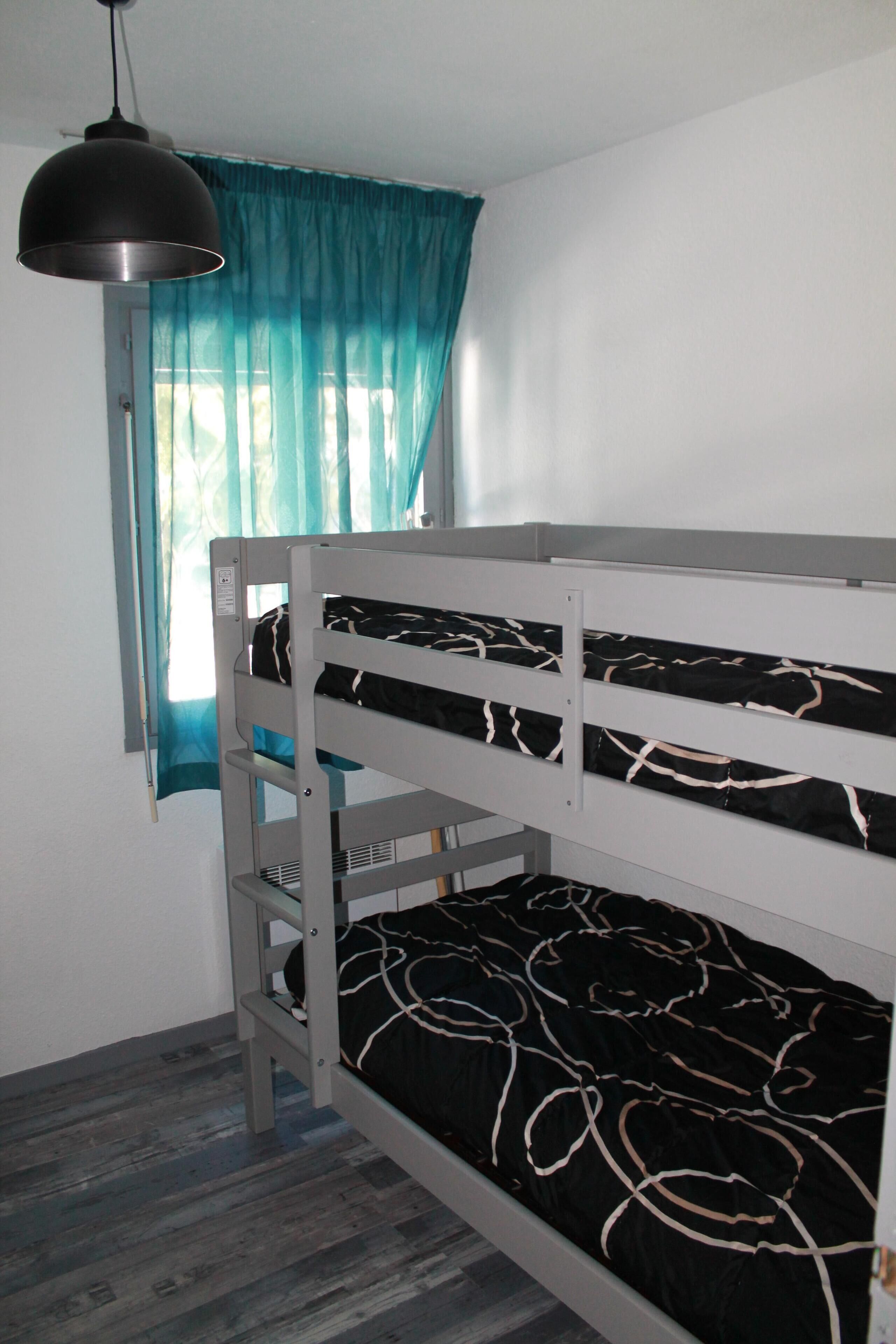 A bunk bed with a black and white patterned mattress, a grey metal frame, and a pendant light above.
