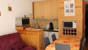 Une cuisine compacte dotée de meubles en bois, d’un four à micro-ondes, d’une machine à café et d’un coin repas avec une table et des chaises.