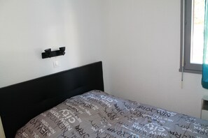 Un dormitorio con cabecera negra, cama con colcha estampada, lámpara de pared y ventana con cortina.