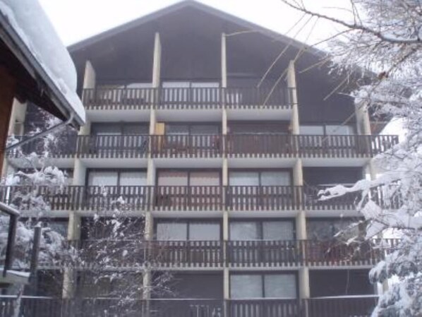 Un edificio de varios pisos con balcones, rodeado de árboles cubiertos de nieve.
