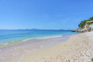 A beach with pebbles, clear water, and a building with a roof on the right. - Fully Renovated Beachfront Dina: A/C, Private Terrace, WiFi (Gimari)