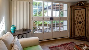 Una habitación con un sofá, una mesa con un florero, un ventanal con vistas al exterior y un armario.