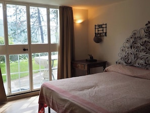 A bedroom with a bed, a desk, a chair, and a view through a large window.