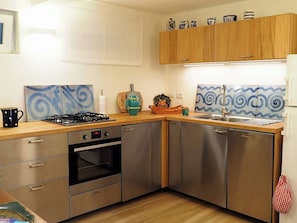 A compact kitchen with stainless steel appliances, wooden cabinets, and decorative tiles.