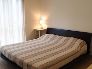 Ein Bett mit einem gestreiften Überwurf, ein Nachttisch mit einer Lampe und ein Fenster mit Vorhängen.