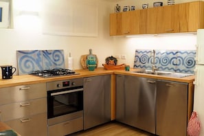 Une cuisine de taille réduite, dotée d’appareils électroménagers en acier inoxydable, de meubles en bois et de carreaux décoratifs.