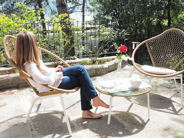 A person seated on a wicker chair with a glass table in an outdoor setting.