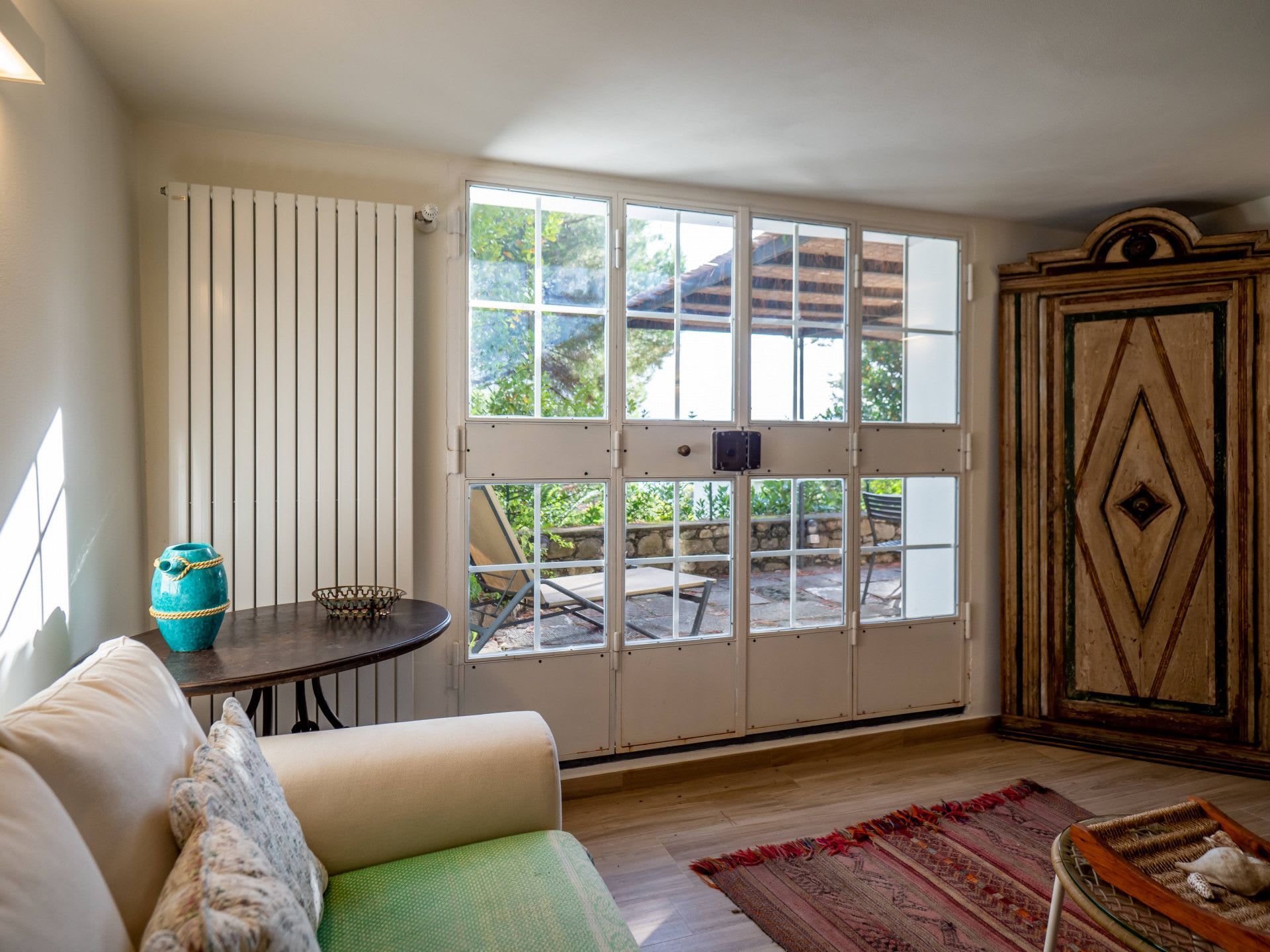 Ein Zimmer mit einer großen Schiebetür, einem runden Tisch mit einer blauen Vase, einem grünen Sofa und einem gemusterten Teppich.
