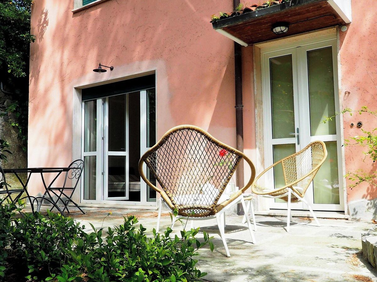 Un bâtiment à la façade rose, avec une porte d’entrée en verre et deux chaises en osier à l’extérieur.