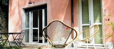 Un bâtiment à la façade rose, avec une porte d’entrée en verre et deux chaises en osier à l’extérieur.