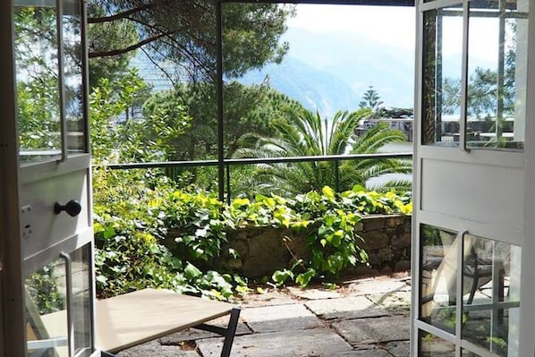 An open door to a balcony with a view of greenery and a stone wall.