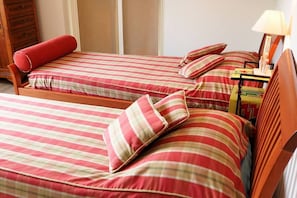 Deux lits simples avec une literie à rayures, une tête de lit en bois et une table de chevet avec une lampe.