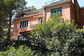 Un immeuble à plusieurs étages, doté de balcons, d’un toit plat et d’un feuillage dense à l’avant.