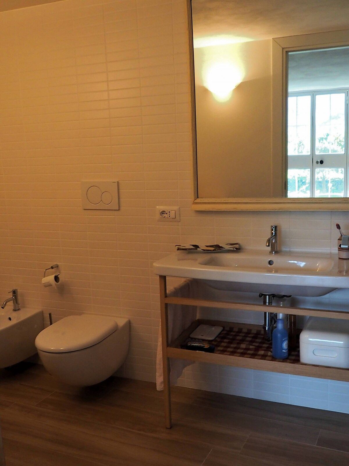 A bathroom with a white toilet, a bidet, a sink with a mirror above it, and a towel rack.