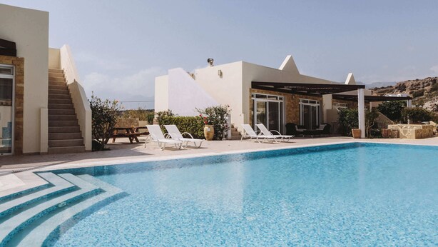 A modern pool area with a clear blue pool, white lounge chairs, and a covered seating area. - Family Getaway with Pool in Southern Crete (Lagkada)