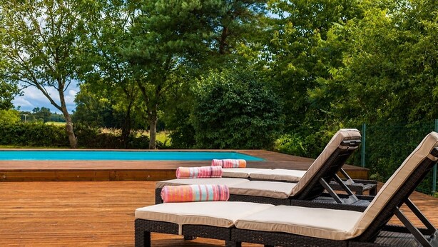 Une terrasse en bois avec deux chaises longues et une piscine.
