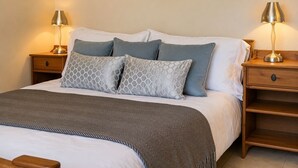 Un lit bien fait, recouvert d’une couverture à motifs gris et blancs, avec deux oreillers gris et une table de chevet en bois sur laquelle se trouve une lampe.