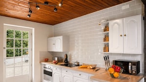 Une cuisine avec des meubles blancs, un plan de travail en bois et une vue sur la verdure à l’extérieur.