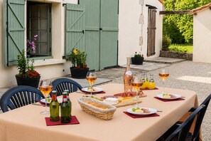 An outdoor dining area with a table set for a meal, including plates of food, bottles of wine, and a basket of bread. - Beautiful French Farmhouse with Private Heated Pool | Sleeps 8 (Genouillé)