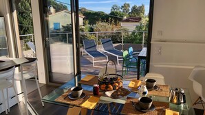 Zona pranzo moderna con tavolo in vetro, sedie bianche e vista sul patio esterno con poltrone relax.