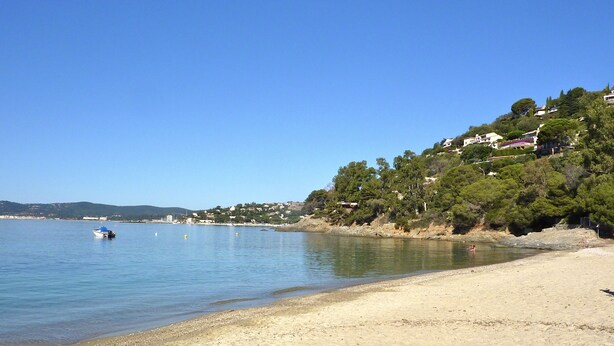 Una spiaggia sabbiosa con un mare calmo, una barca e case su una collina sullo sfondo.
