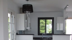 Eine moderne Küche mit weißen Schränken, einer schwarzen Arbeitsplatte und einem Fenster. Es gibt einen Essbereich mit einem weißen Tisch und schwarzen Stühlen.