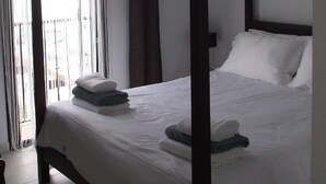 Ein Himmelbett mit Deckenventilator, weißen Leinen und Blick durch transparente Vorhänge nach draußen.