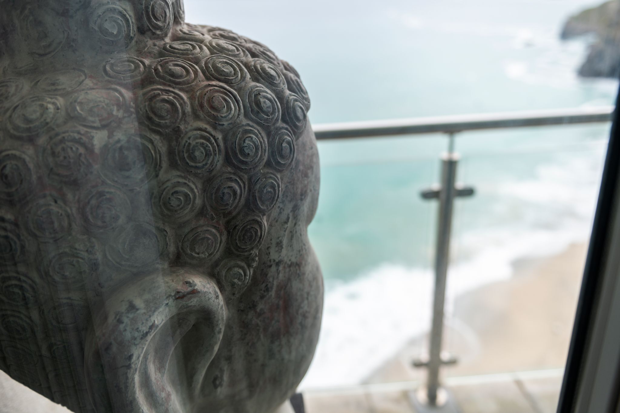 Een detailopname van een sculptuur met een spiraalpatroon, zichtbaar vanaf een balkon met uitzicht op de oceaan.