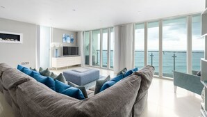Ett modernt vardagsrum med ett stort fönster med utsikt över havet, en platt-TV och en minimalistisk, vit TV-bänk.