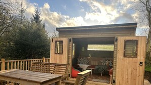 A wooden deck with a table and chairs, a bench, and a small wooden structure with a bench inside. - 5* STUNNING LUXURIOUS BEAMED COTTAGE - SECLUDED PEACEFUL PEAK DISTRICT LOCATION (Leek)