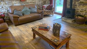 A cozy living room with a stone wall, a brown leather sofa, a wooden coffee table, and a fireplace. - 5* STUNNING LUXURIOUS BEAMED COTTAGE - SECLUDED PEACEFUL PEAK DISTRICT LOCATION (Leek)