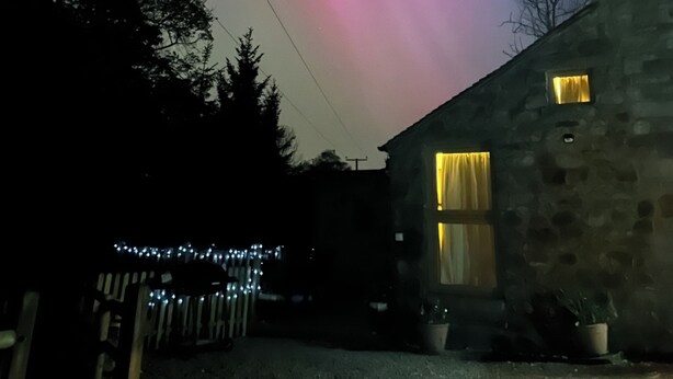A stone building with a window illuminated by yellow light, a clear night sky, and a faint aurora display. - 5* STUNNING LUXURIOUS BEAMED COTTAGE - SECLUDED PEACEFUL PEAK DISTRICT LOCATION (Leek)