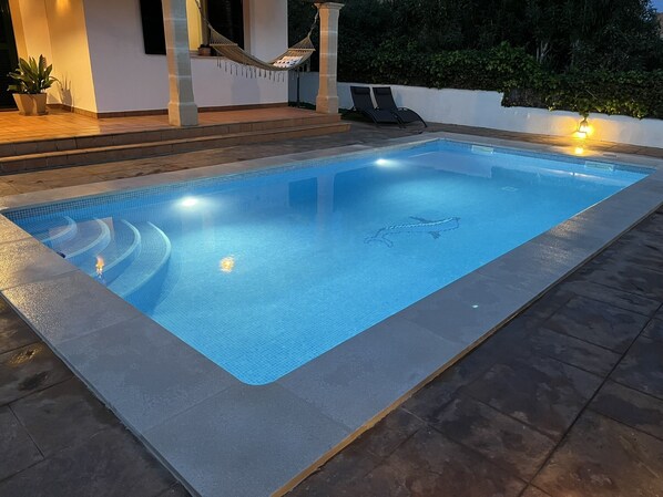 Una piscina rectangular con borde de azulejos, rodeada de baldosas de piedra.