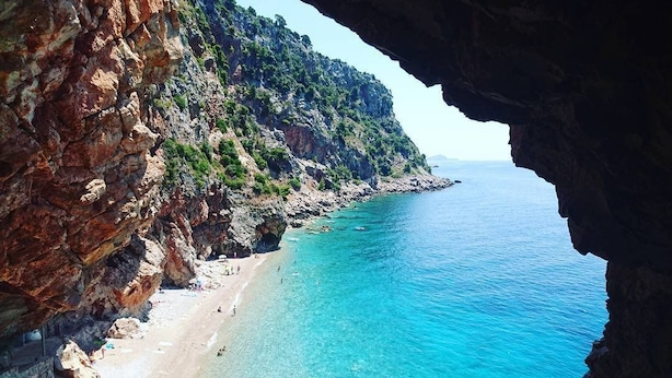 Una playa costera con aguas turquesas cristalinas y acantilados rocosos.