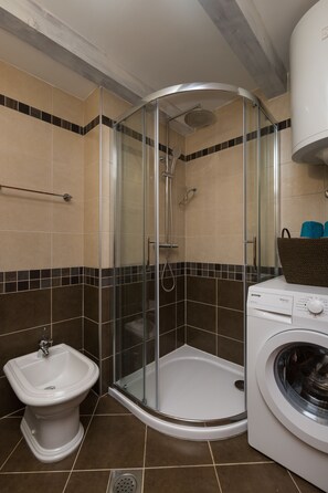 A bathroom with a glass-enclosed shower, a bidet, and a washing machine. - Villa Guardian Heritage (Konavle)