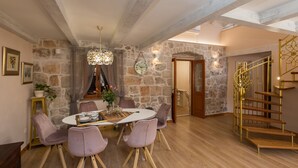 Un área de comedor con pared de piedra, escalera de madera y una araña.