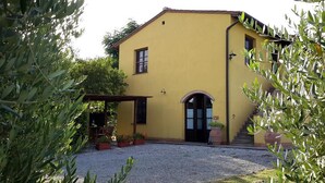A yellow building with a covered entrance, potted plants, and a gravel driveway. - Villa with pool in Tuscany, close to San Gimignano and Volterra  (Villamagna)