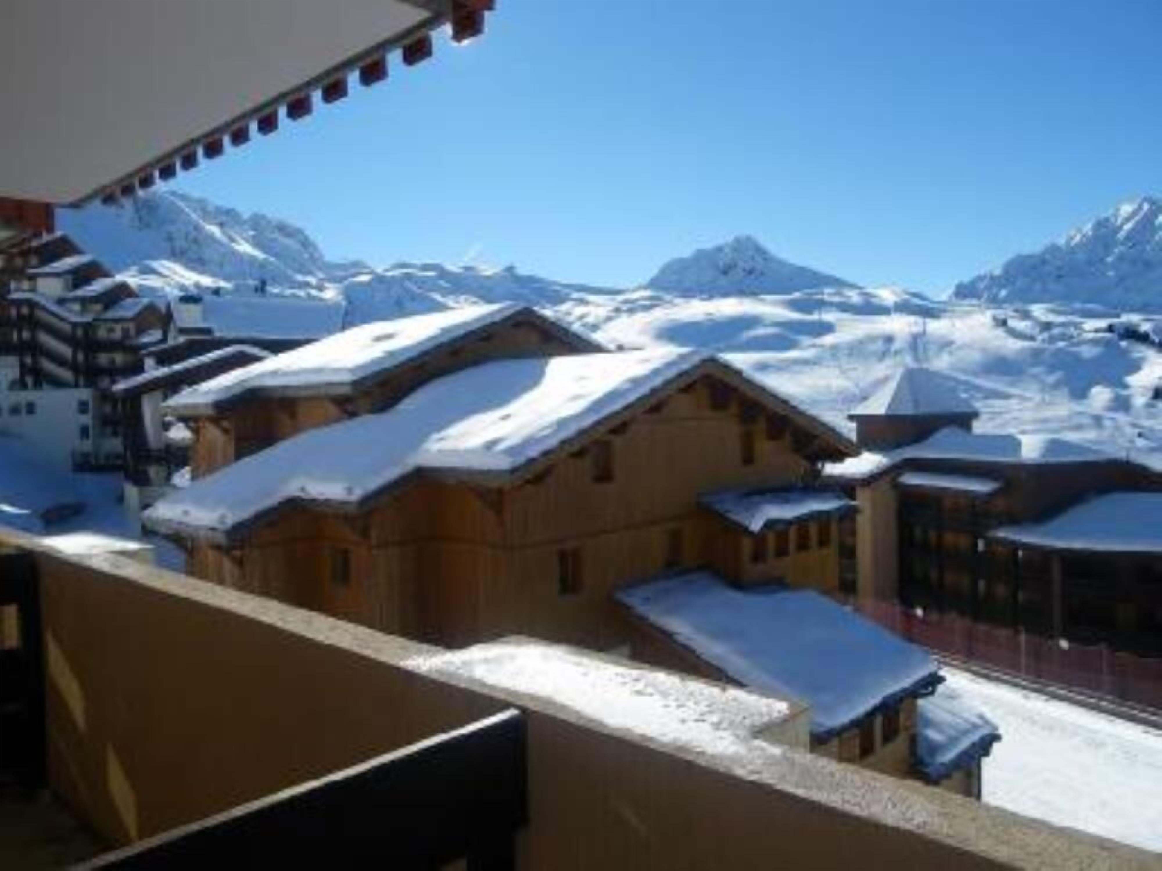 Un village de montagne enneigé, avec des bâtiments en bois et un ciel bleu azur.