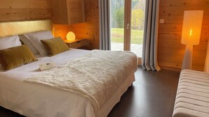 Camera da letto in una baita di legno con un letto grande, un comodino con una lampada e vista sulla foresta dalla finestra.