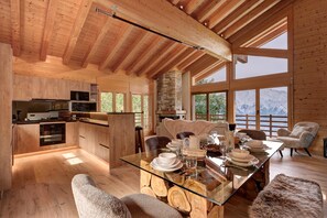 Cozinha ampla com eletrodomésticos modernos, área de jantar com mesa de vidro e grandes janelas com vista para as montanhas.