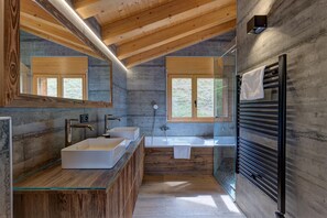 Uma casa de banho moderna com lavatório de vidro, duas pias, um espelho grande, uma banheira e um porta-toalhas.