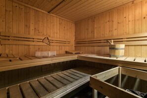 En träbeklädd bastu med bänkar och en träspänd hink.