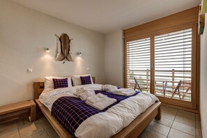 Camera da letto con un letto grande, testiera in legno e vista su un balcone attraverso finestre a tutta parete.
