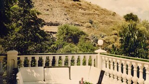 Un patio con un sofá blanco, una mesa con planta en maceta y vistas a una colina.