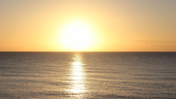 Un coucher de soleil sur une mer calme, avec un horizon dégagé.